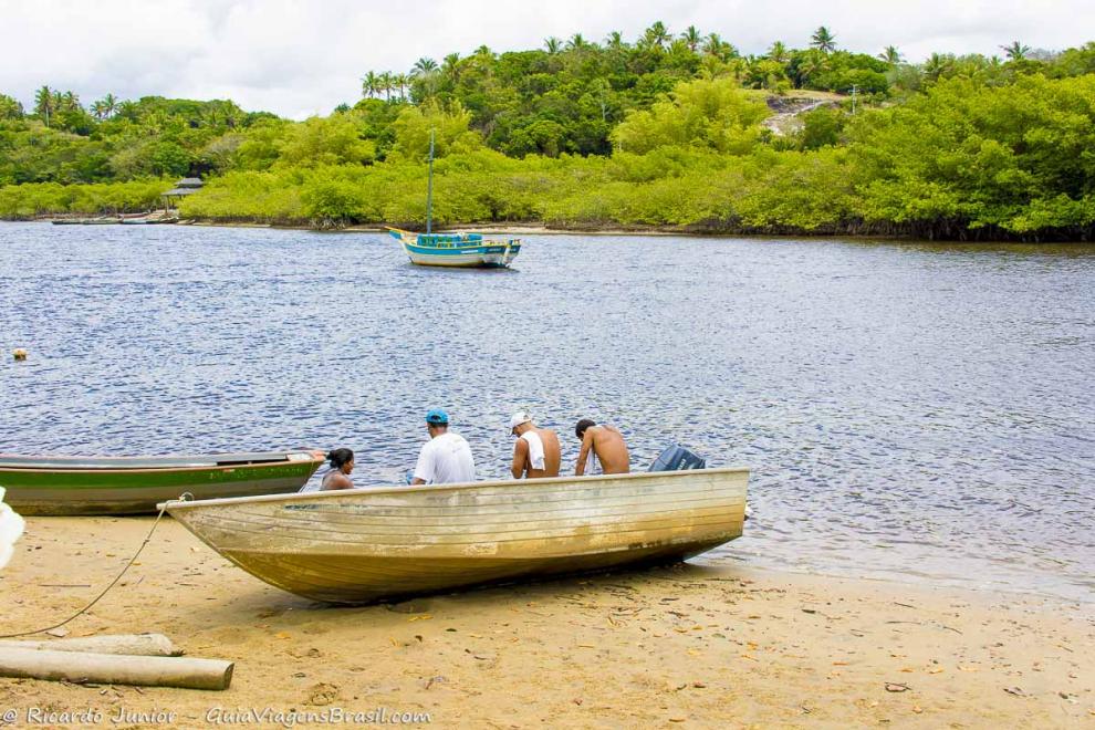 Imagem de pescadores sentados no barco parado na areia da costa do rio Caraiva.